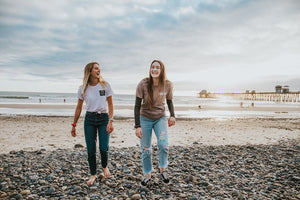 Two young women walking on the beach and wearing colorful Nöz sunscreen made of reef-safe ingredients. 